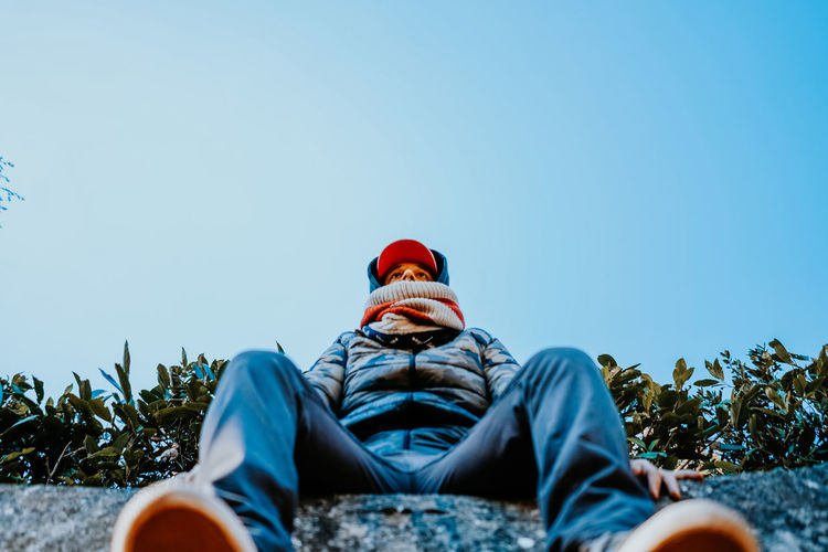 Low section of man sitting against clear sky