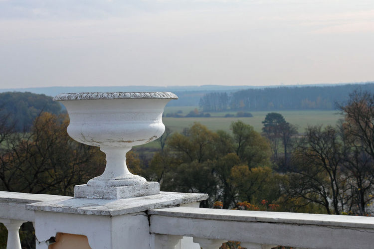 Decorative urn on railing by trees against clear sky