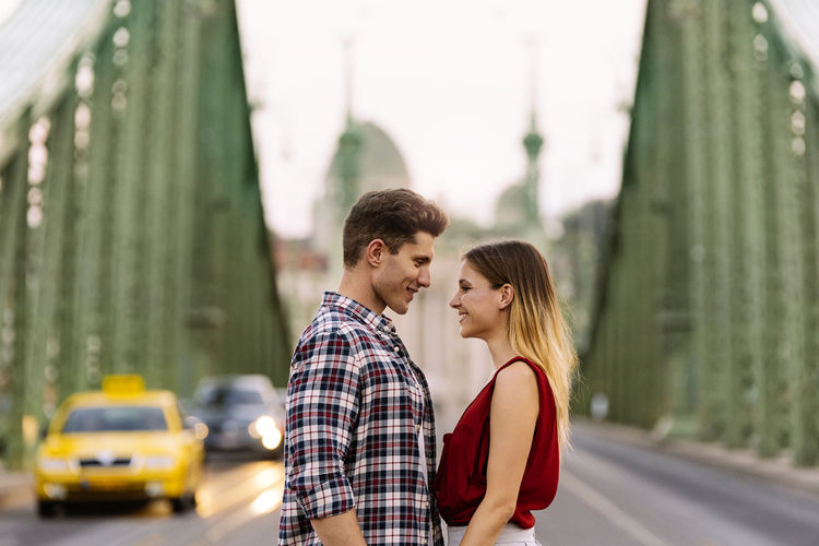 Side view of couple standing on bridge in city