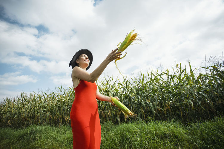 Happy woman juggling corns at field on sunny day