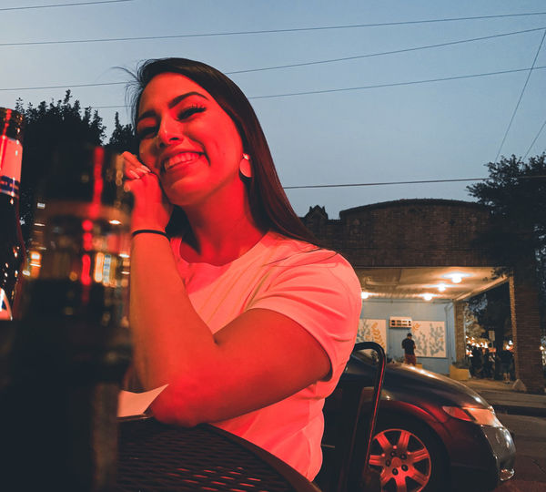 Portrait of young woman drinking beer in city at night