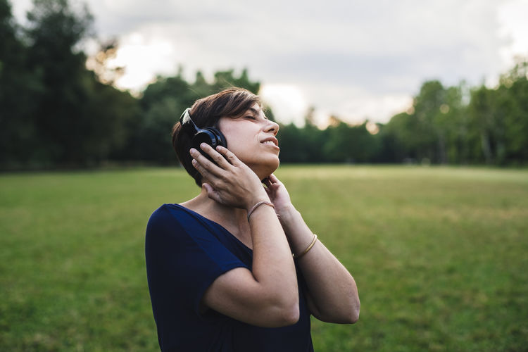 Woman listening music on field against sky