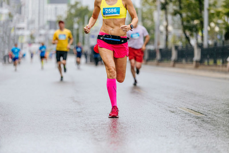 Legs female runner in pink compression socks run in rain on wet road marathon