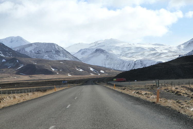 Road leading towards snowcapped mountains against sky