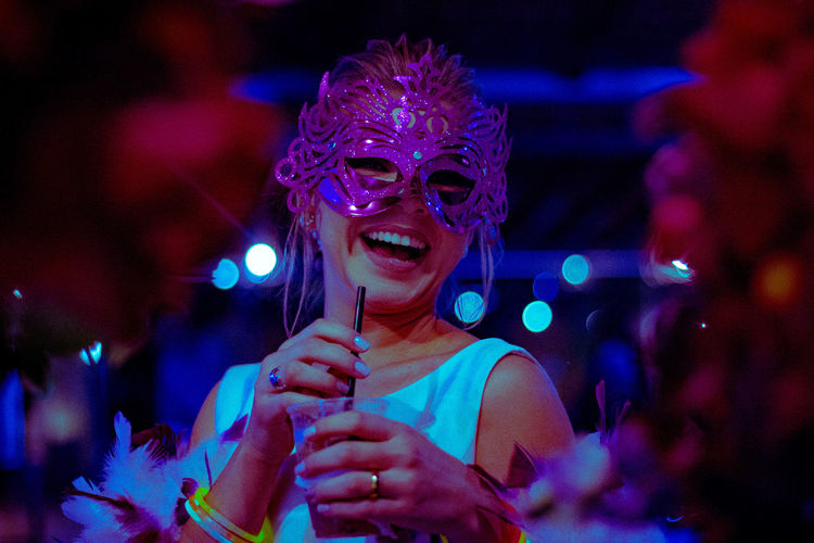 Cheerful woman wearing eye mask holding drink during party