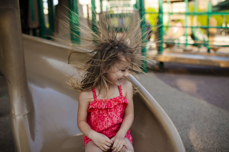 Happy girl playing flicking hair while sitting on slide