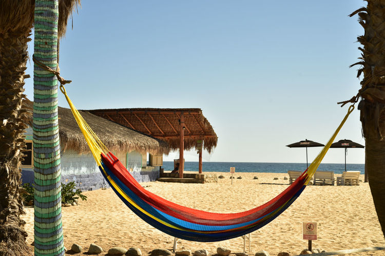 Rainbow color hammock  palm tree trunks on beach with beach bar and palapa in background
