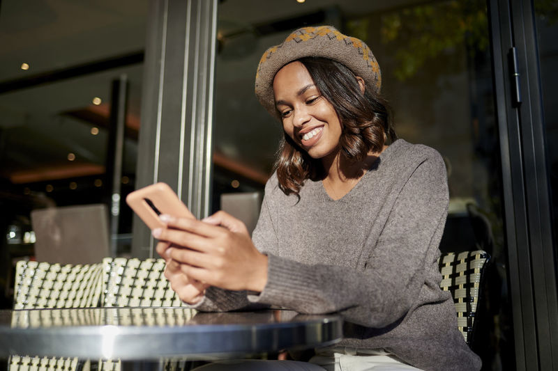 Smiling woman using smart phone at sidewalk cafe