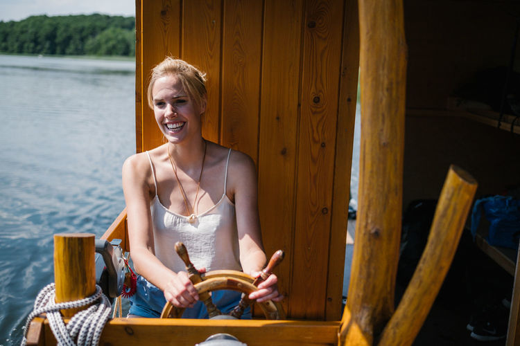 Smiling woman sitting by wheel in boat on lake