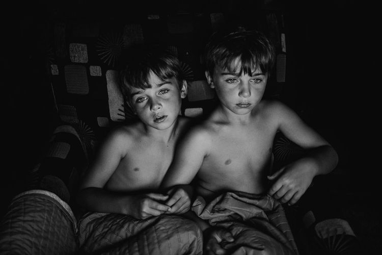 Portrait of shirtless boys sitting on bed at home