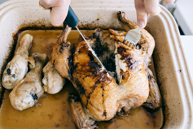 High angle view cropped hand cutting roasted chicken in tray