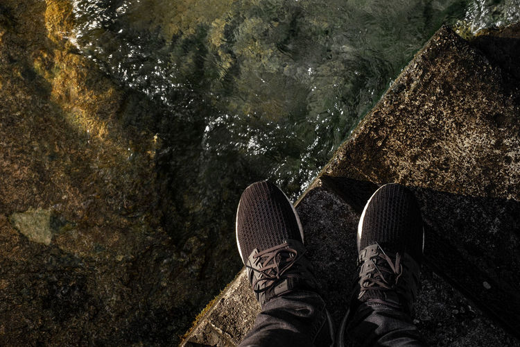 Low section of person standing on retaining wall by lake