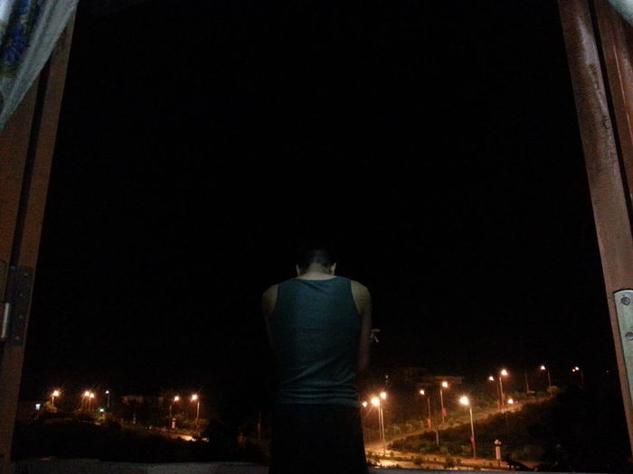 REAR VIEW OF MAN STANDING ON NIGHT