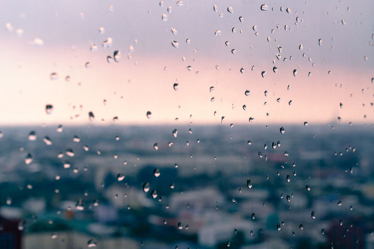 Full frame shot of wet glass window with urban background