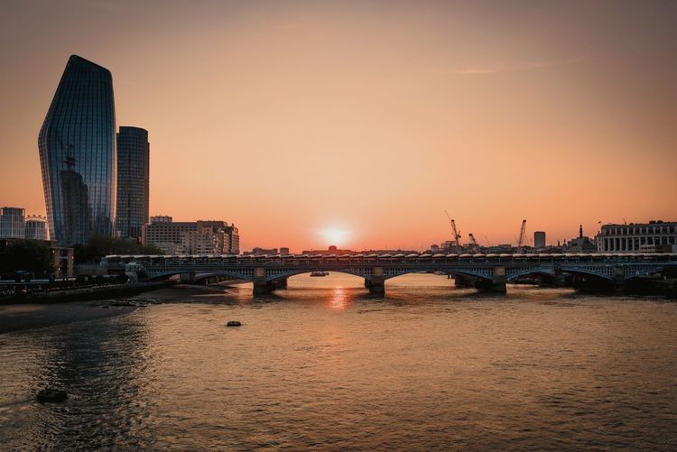 Bridge over river against buildings during sunset