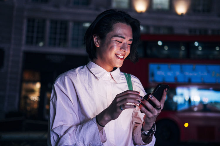 Smiling handsome man surfing net through mobile phone in city at night