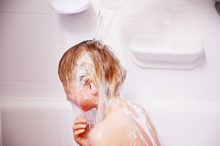 Side view of a boy bathing under shower