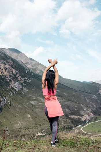 Rear view of woman with arms raised standing against mountains