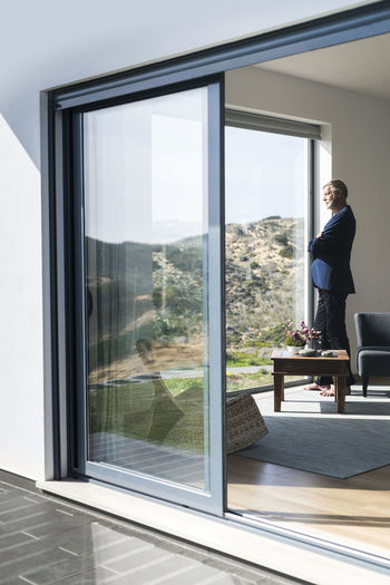 Senior businessman standing at panorama window looking out barefoot