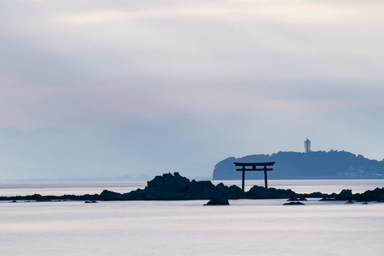 Light ray over the sea with the view of torii gate and light house in the distance.