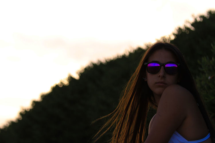 Portrait of teenage girl wearing sunglasses against sky during sunset