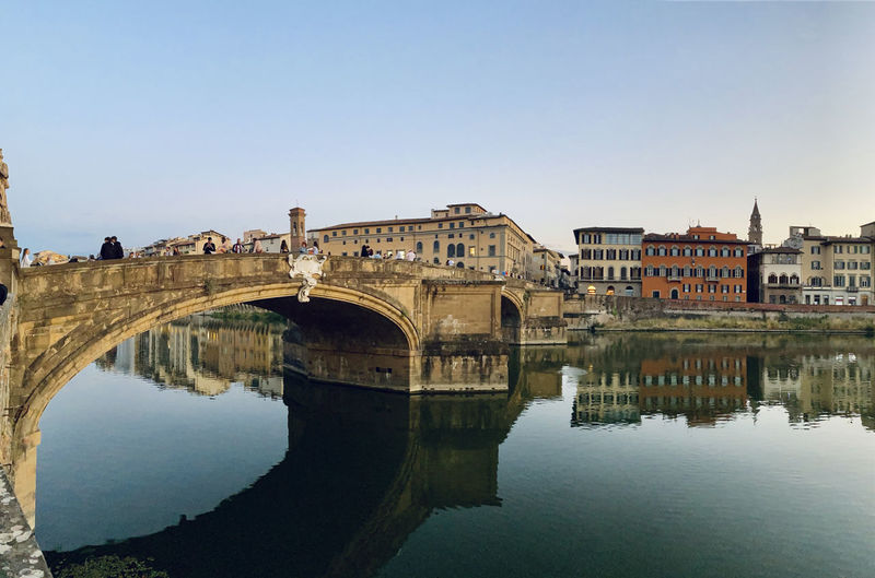 Arch bridge over river by buildings against clear sky
