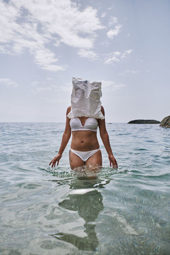 A woman coming out of the sea with a bag on her head. recycling concept