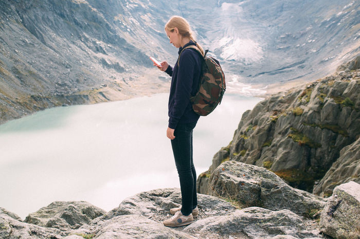 Young woman looking at phone with mountain lake seen below