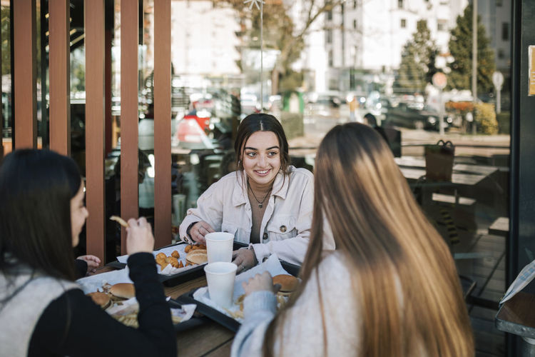 Female friends talking while having fast food at outdoor restaurant