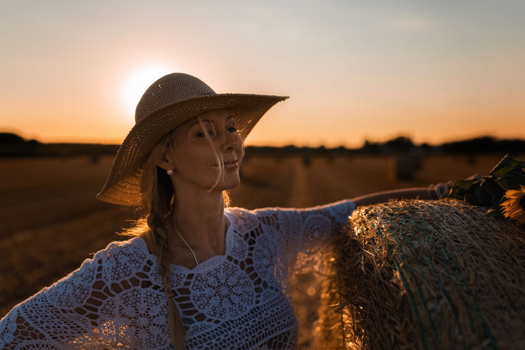 Portrait of woman wearing straw hat looking away against sky during sunset