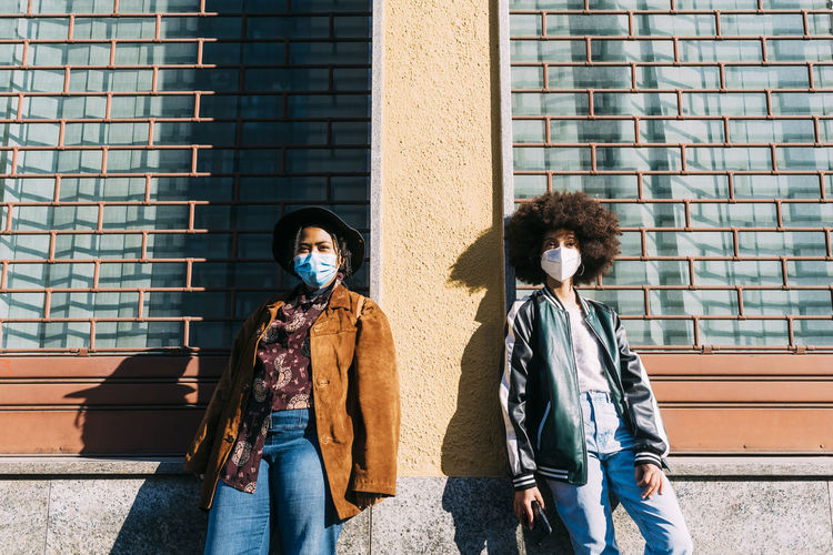Young women wearing protective face masks standing with social distance in front of building