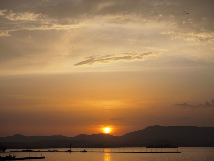 Silhouetted jetty with boats and mountain at dusk