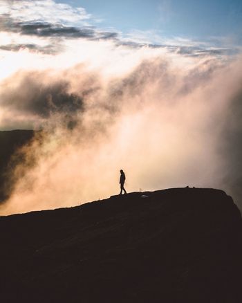 Silhouette man walking on mountain against cloudscape