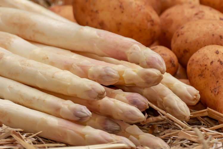 Fresh raw organic white asparagus and potatoes on straw background. asparagus officinalis