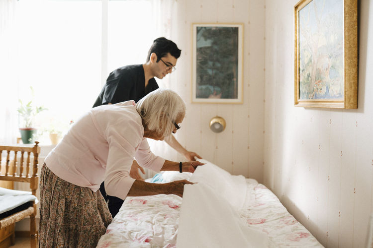Senior woman and male healthcare worker placing blanket on bed at home