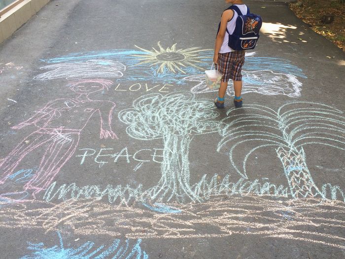 Low section of backpack boy with container standing on chalk drawing