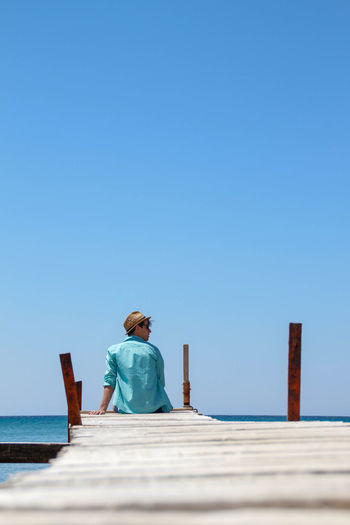 Rear view of woman walking on pier against clear blue sky