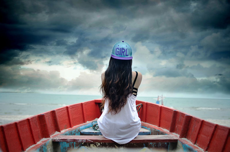 Rear view of woman sitting in boat on sea against cloudy sky