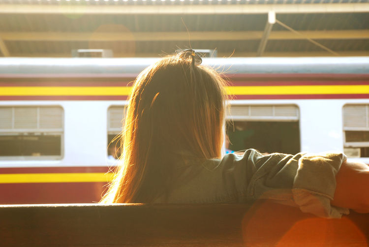 Rear view of young woman sitting on railroad platform
