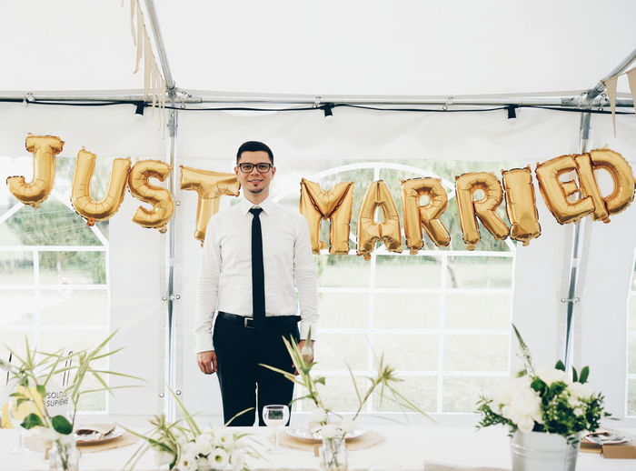Portrait of smiling bridegroom standing against text in tent