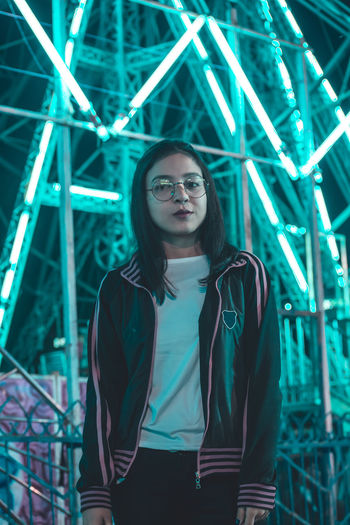 Portrait of young woman standing against illuminated ride at night