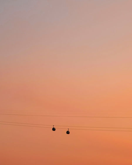 Low angle view of silhouette overhead cable cars against orange sky during sunset