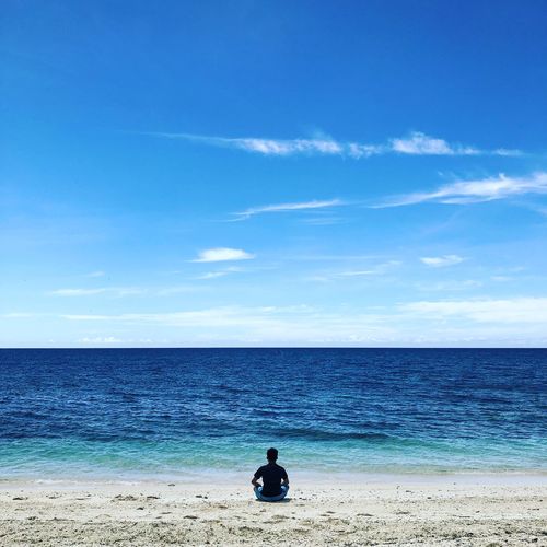 Rear view of man sitting on beach against sky