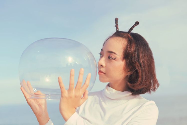 Young woman holding crystal ball against sky
