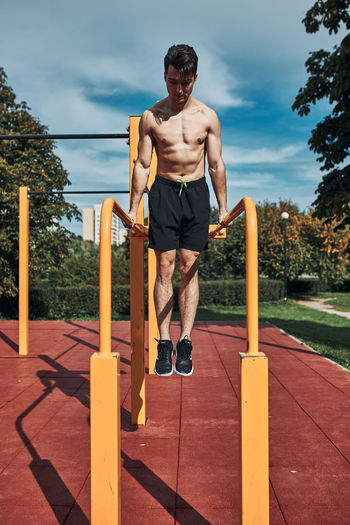 Young shirtless bodybuilder doing dips on parallel bars during his workout in a calisthenics park