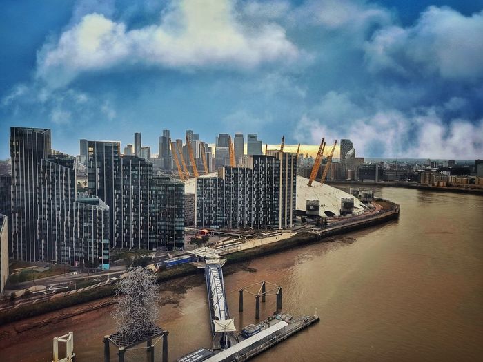 Modern buildings by river against sky in city