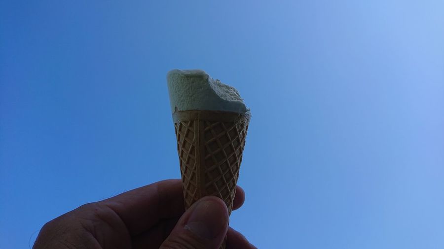 Hand holding ice cream against blue sky
