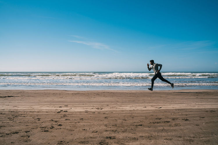 Full length of man running on beach against sky