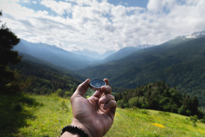 Strong male hand holds a compass against the background of a lush green field and forest with