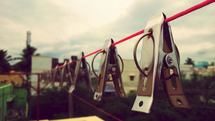 Close-up of clothespins hanging on clothesline against sky